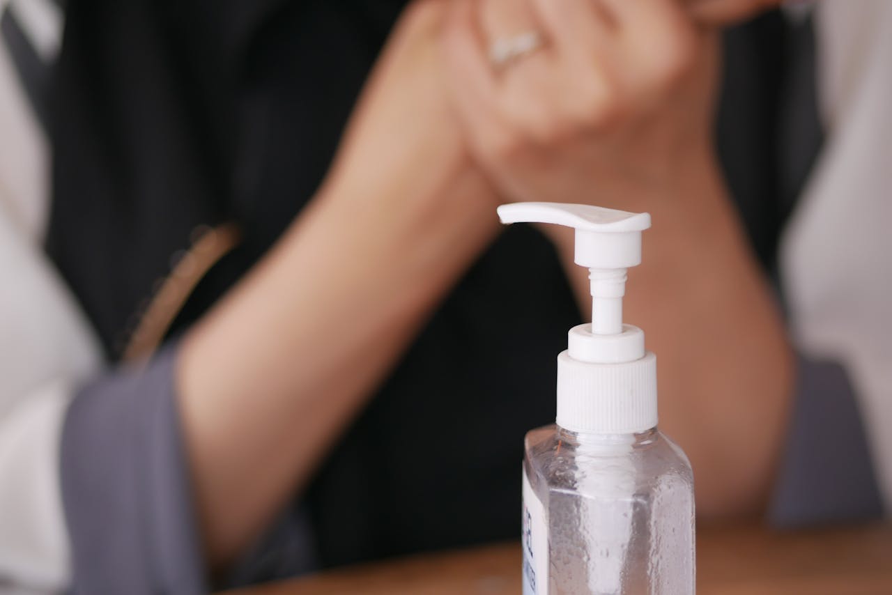Focused image of a liquid soap dispenser with blurred hands in the background.